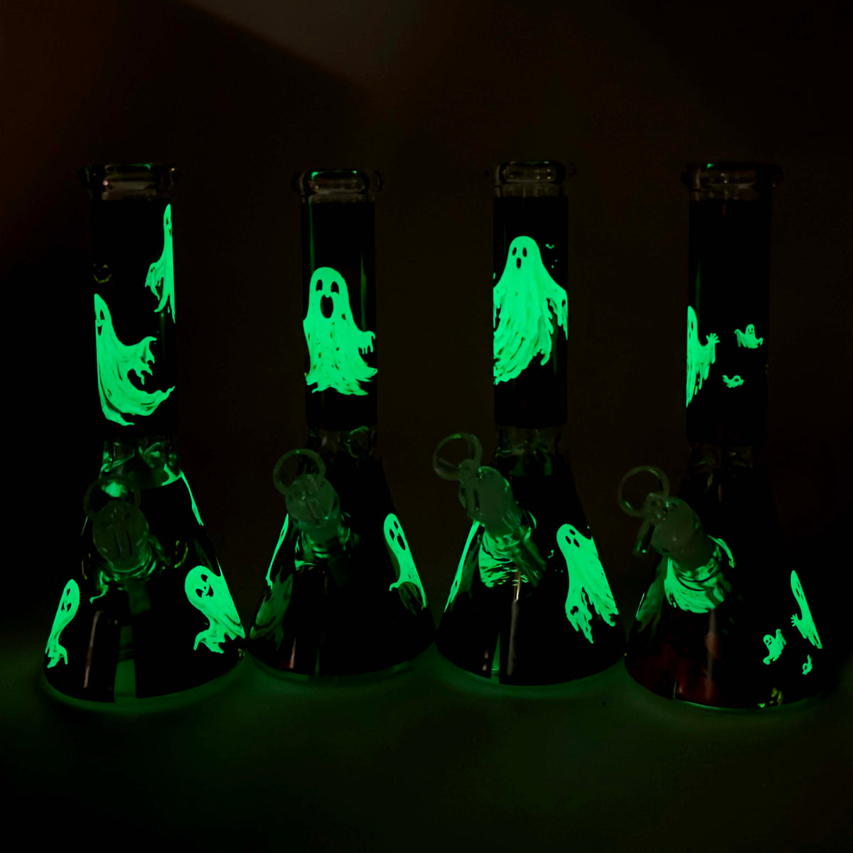 Four cute ghost beaker bongs in darkness with ghost graphics glowing bright green